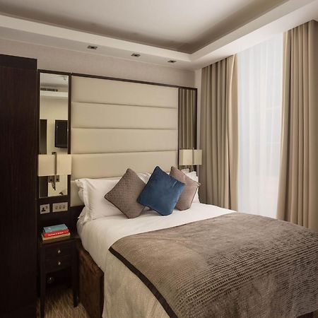 فندق Montcalm Brewery Townhouse لندن المظهر الخارجي الصورة The image shows a cozy bedroom. It features a comfortable double bed with a light-colored duvet and decorative pillows in shades of blue and gray. The headboard is upholstered in a soft material, and there are bedside lamps on either side of the bed.