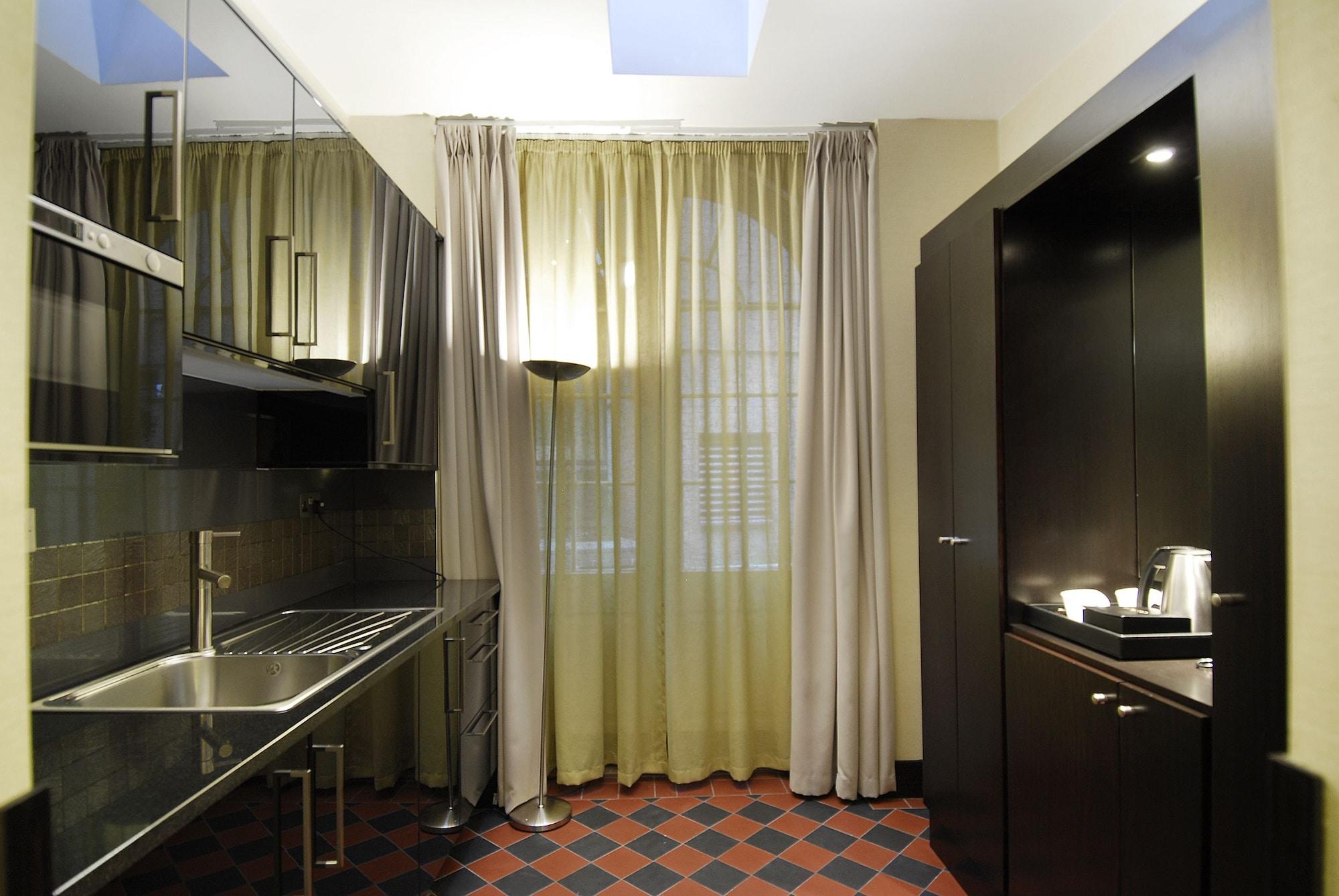 فندق Montcalm Brewery Townhouse لندن المظهر الخارجي الصورة The photo shows a modern kitchen space. On the left side, there is a sleek countertop and kitchen cabinets in a dark finish. The backsplash appears shiny, reflecting the surroundings. To the right, there is a tall black cabinet. A window is covered w