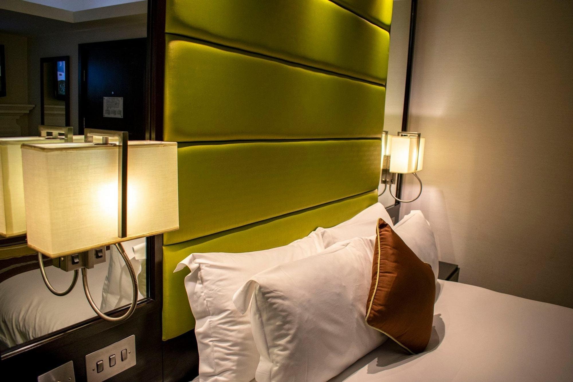 فندق Montcalm Brewery Townhouse لندن المظهر الخارجي الصورة The photo shows a modern hotel room with a stylish design. The focal point is a large bed with white pillows and a decorative brown pillow. The headboard is bright green and has a textured appearance. On either side of the bed, there are wall lamps t