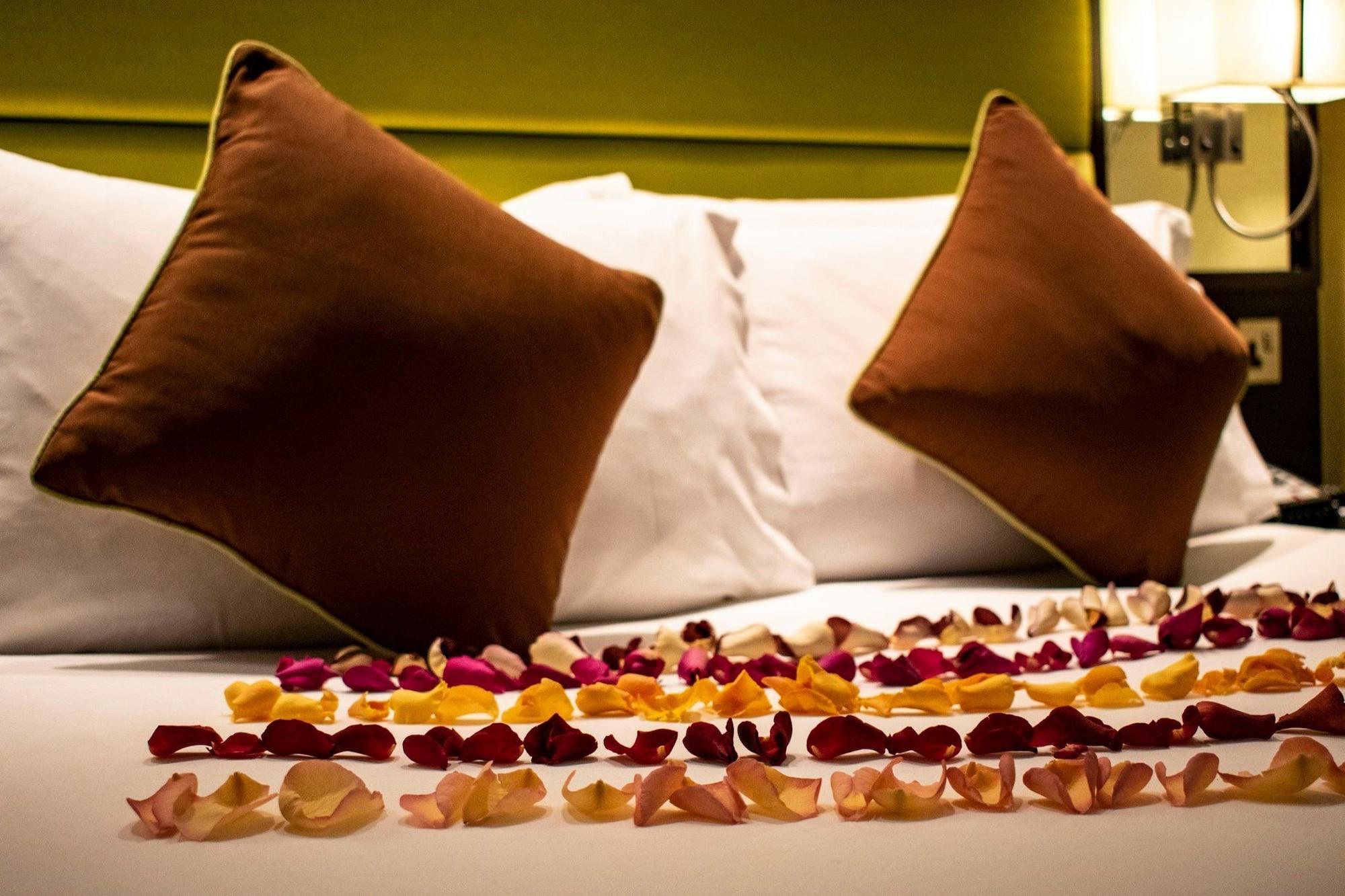 فندق Montcalm Brewery Townhouse لندن المظهر الخارجي الصورة The photo shows a neatly arranged bed with two white pillows and brown decorative cushions. Scattered across the bed is a decorative display of flower petals in various colors, including pink, yellow, and orange, creating a romantic or tranquil ambia