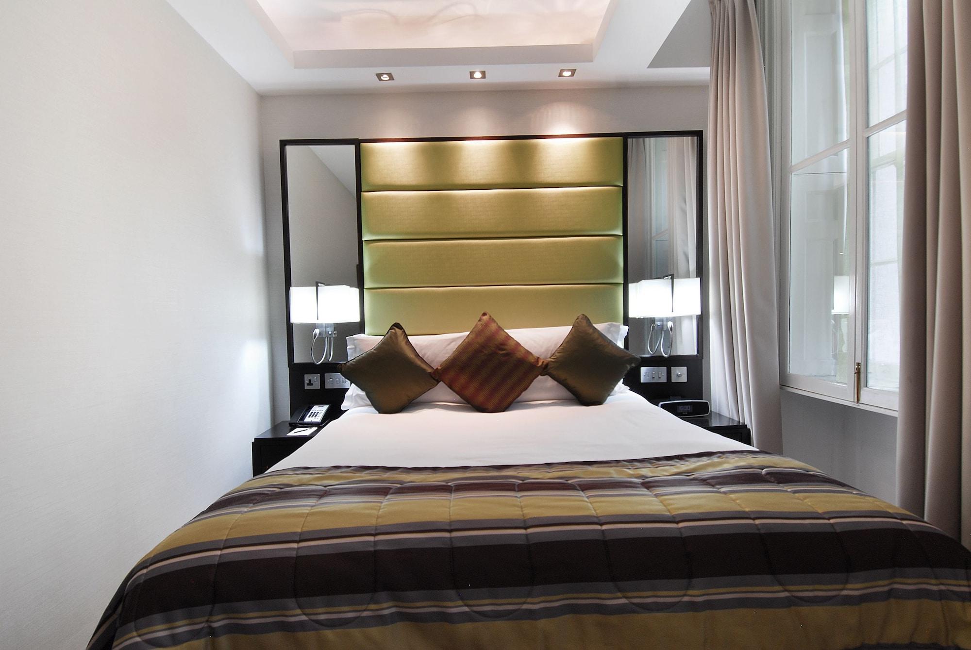 فندق Montcalm Brewery Townhouse لندن المظهر الخارجي الصورة The photo shows a stylishly decorated bedroom. The bed is centered in the room, featuring a white comforter with a plaid pattern in shades of brown and green. There are three decorative pillows on the bed, two in shades of brown and one in dark green