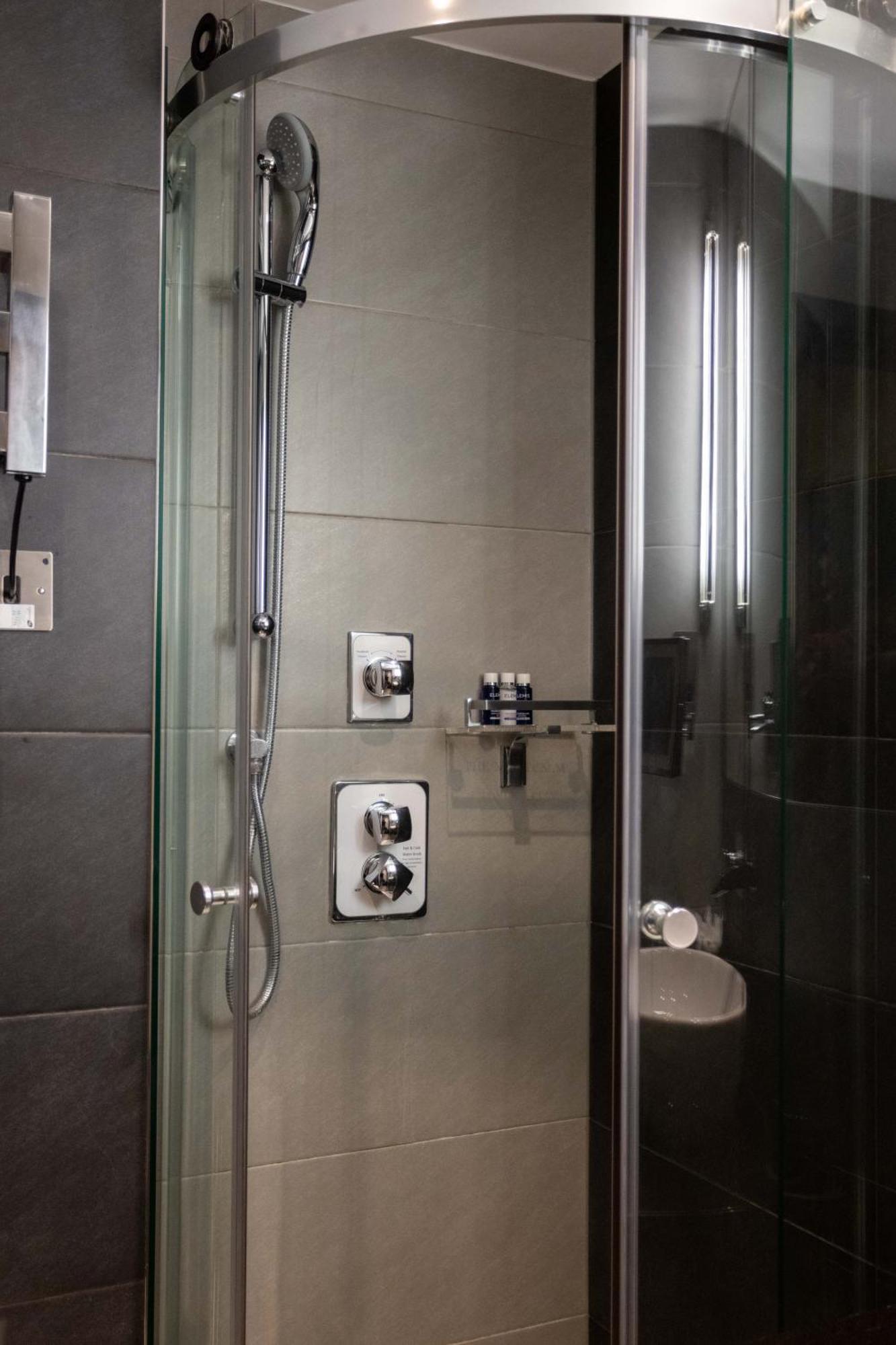 فندق Montcalm Brewery Townhouse لندن المظهر الخارجي الصورة The photo shows a modern shower area. It features glass panels and tiled walls in a neutral color palette, creating a sleek and contemporary look. There are two main control panels for adjusting the water temperature and pressure, with various knobs 