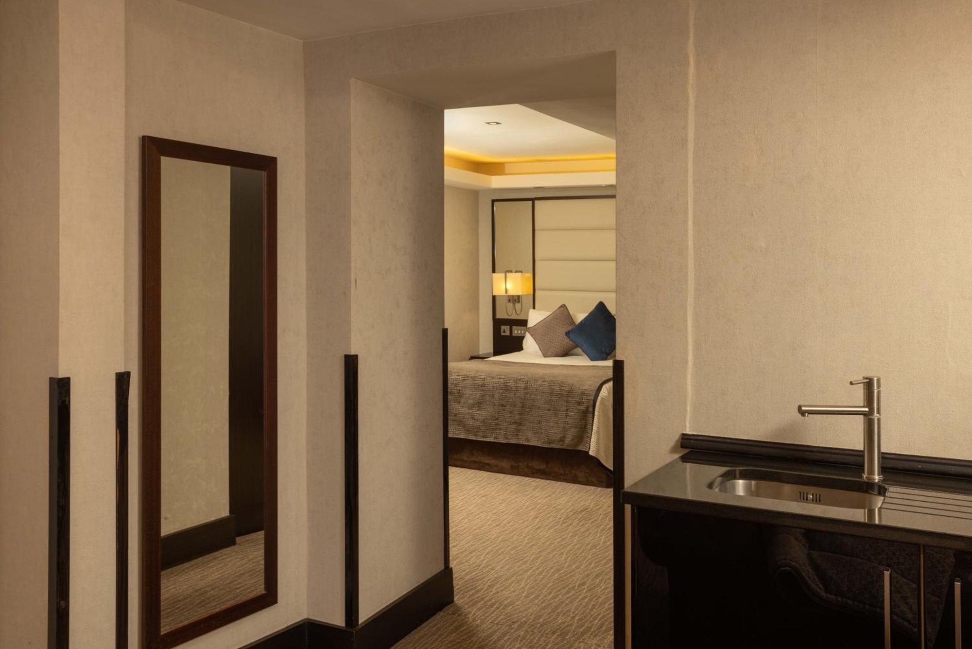 فندق Montcalm Brewery Townhouse لندن المظهر الخارجي الصورة The photo shows an interior space that appears to be part of a hotel room or suite. There is a doorway leading into a bedroom area, where a bed with decorative pillows is visible. In the foreground, there's a tall mirror on the left side and a small 