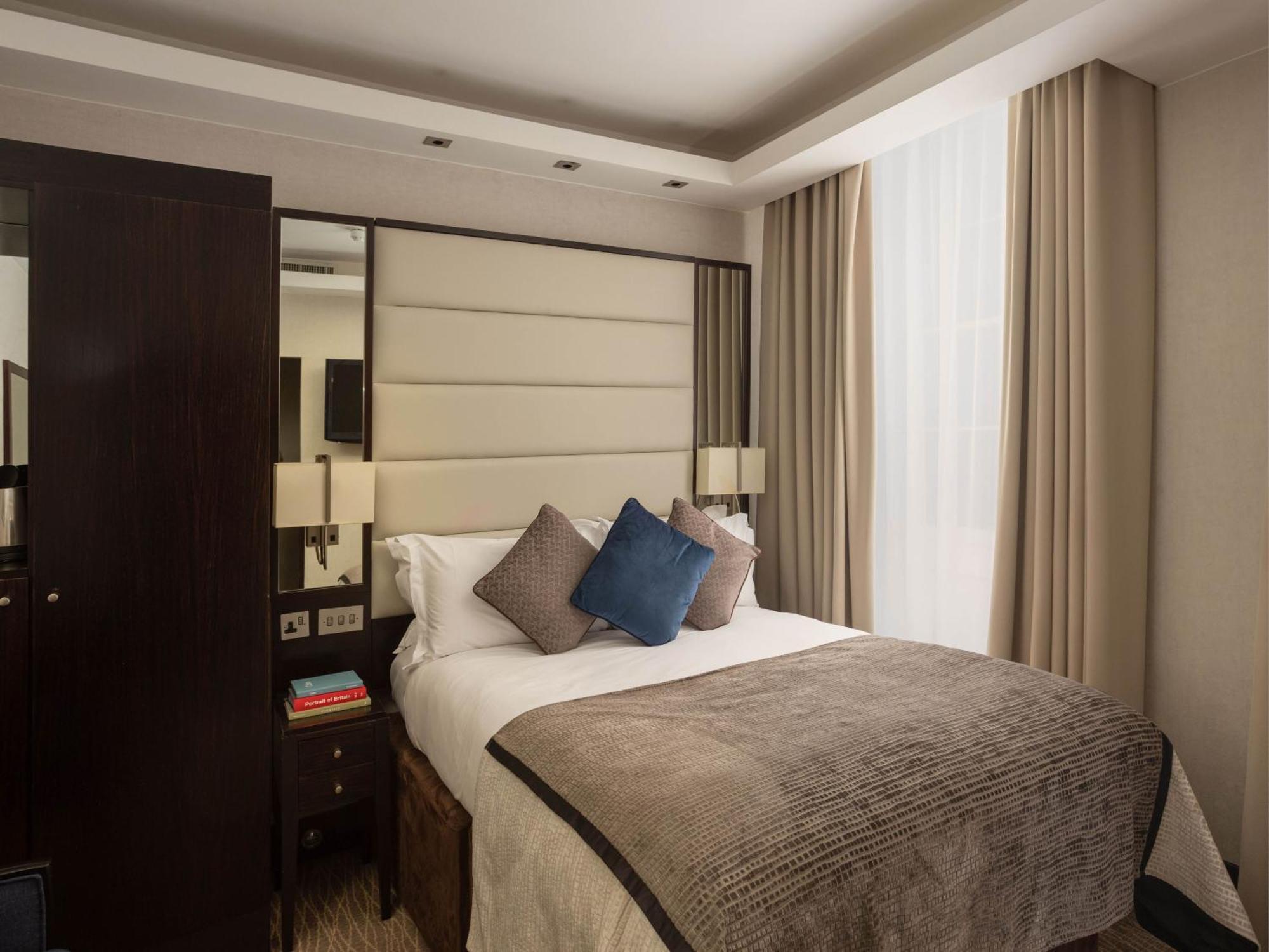 فندق Montcalm Brewery Townhouse لندن المظهر الخارجي الصورة The image shows a cozy bedroom. It features a comfortable double bed with a light-colored duvet and decorative pillows in shades of blue and gray. The headboard is upholstered in a soft material, and there are bedside lamps on either side of the bed.