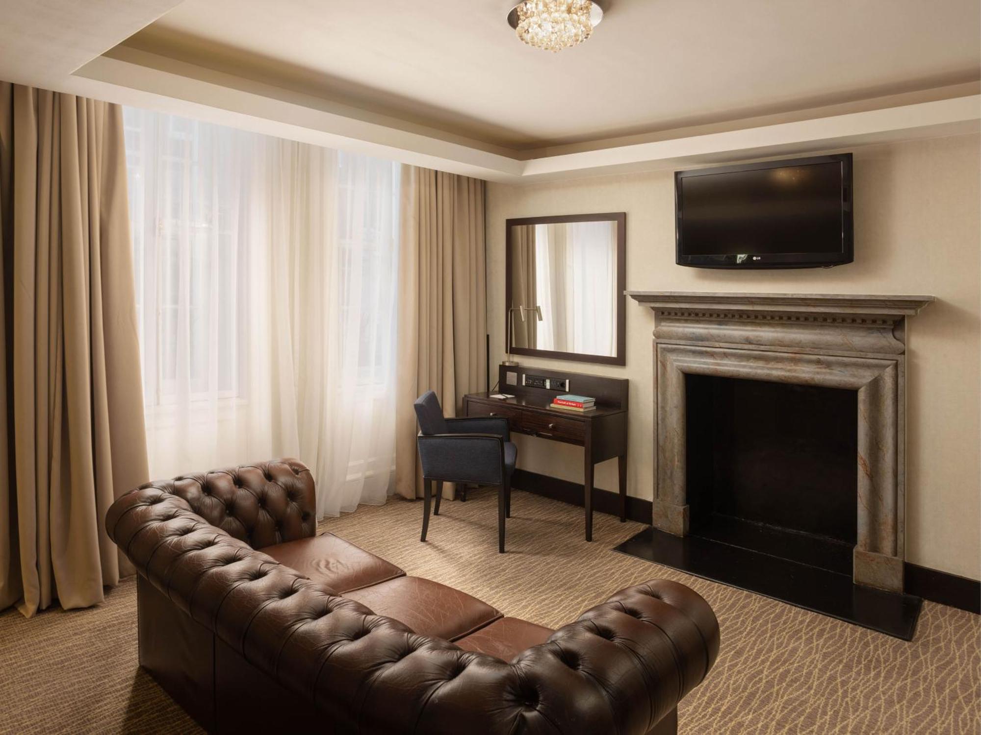 فندق Montcalm Brewery Townhouse لندن المظهر الخارجي الصورة The photo shows a cozy and elegantly designed room. There is a comfortable brown leather sofa with tufted detailing. A small desk and chair are positioned near a mirror, providing a space for work or personal grooming. On the wall, a flat-screen TV i