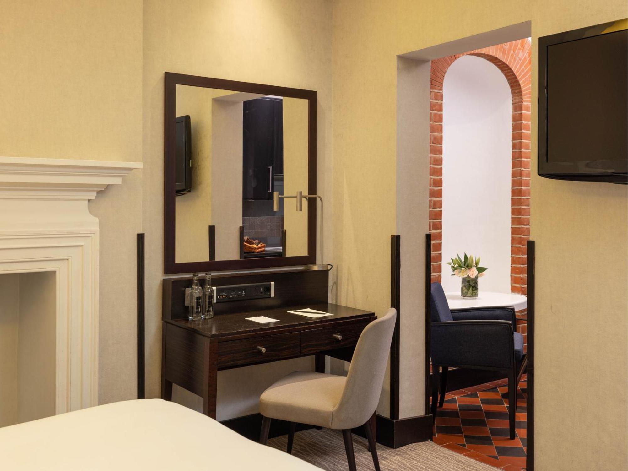 فندق Montcalm Brewery Townhouse لندن المظهر الخارجي الصورة The photo displays a hotel room setup. On the left side, there's a bed with a simple white bedding arrangement. Adjacent to the bed, there's a wooden desk with a chair, along with a mirror above the desk. The desk area is equipped with some glassware