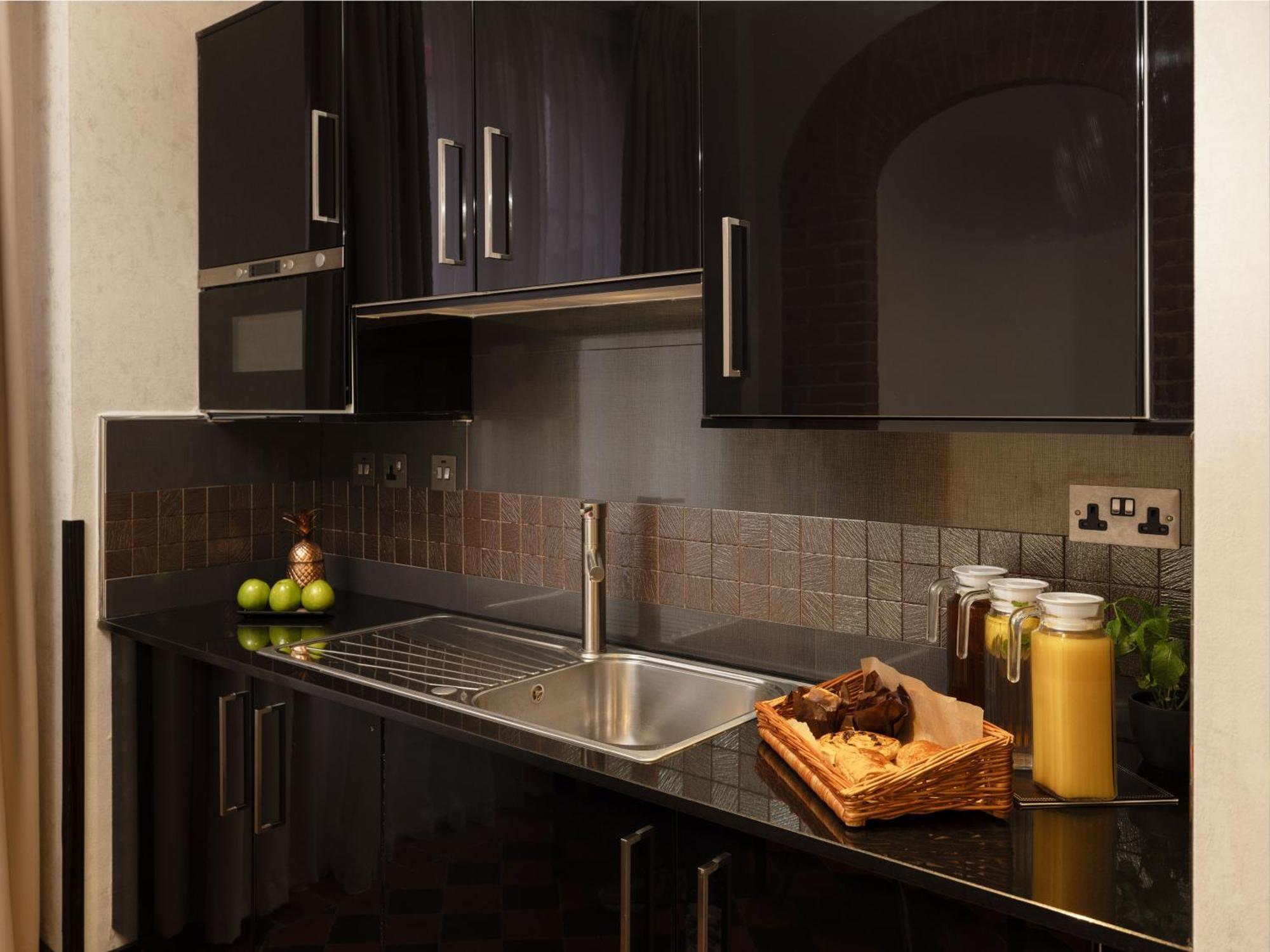 فندق Montcalm Brewery Townhouse لندن المظهر الخارجي الصورة The photo shows a modern kitchen with sleek black cabinetry and a glossy finish. The kitchen features a stainless steel sink with a contemporary faucet, set against a dark, textured countertop. Above the counter, there are cabinets that match the cou