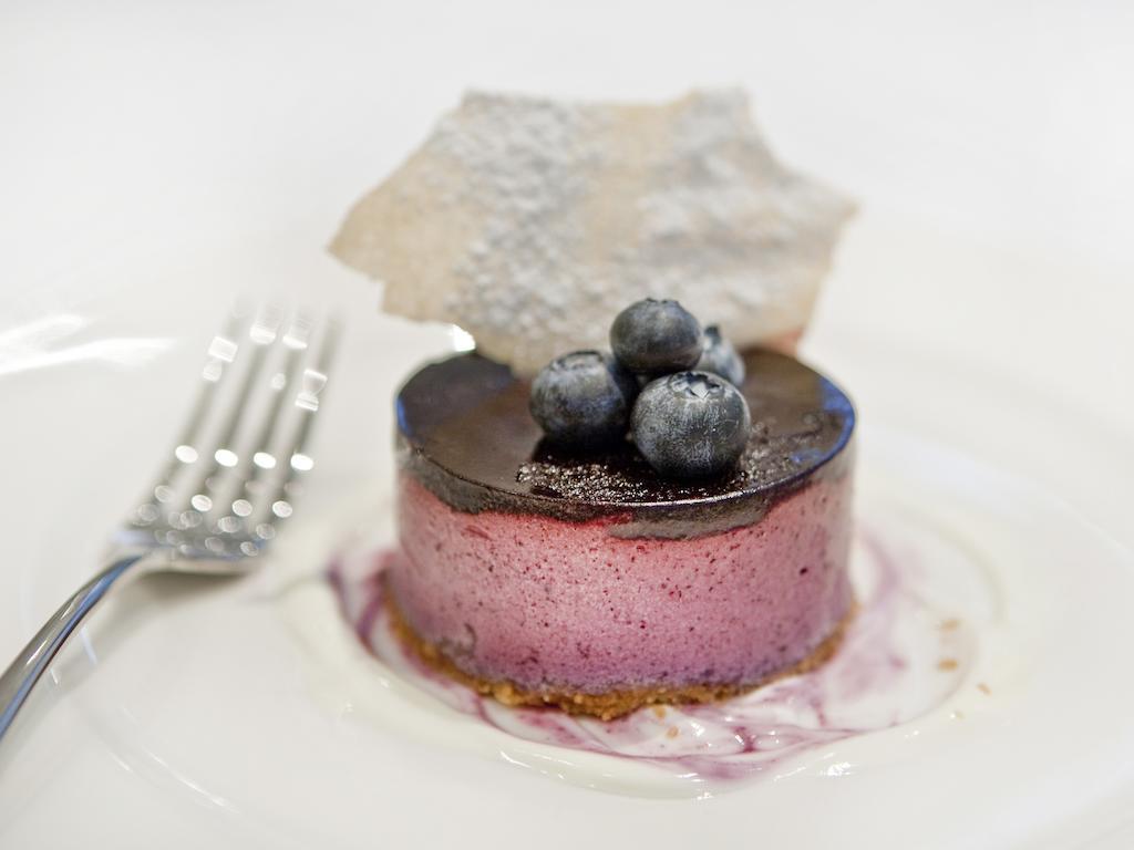 فندق Montcalm Brewery Townhouse لندن المظهر الخارجي الصورة The photo shows a beautifully plated dessert, which appears to be a round cheesecake or mousse. It has a pinkish-purple filling, topped with a glossy dark chocolate layer. Three fresh blueberries sit on top, adding a pop of color. The dessert is acco