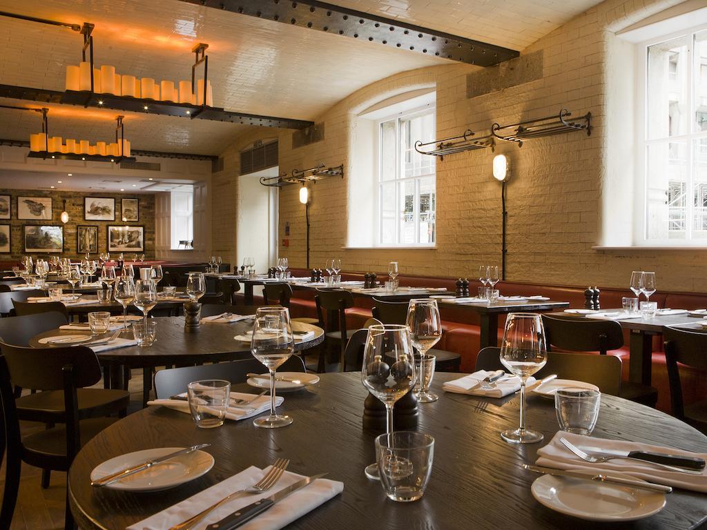 فندق Montcalm Brewery Townhouse لندن المظهر الخارجي الصورة The photo shows a restaurant interior featuring a warm and inviting atmosphere. It has several round wooden tables set for dining, each with neatly arranged plates, utensils, and glasses. The lighting is soft, with overhead fixtures providing a cozy 