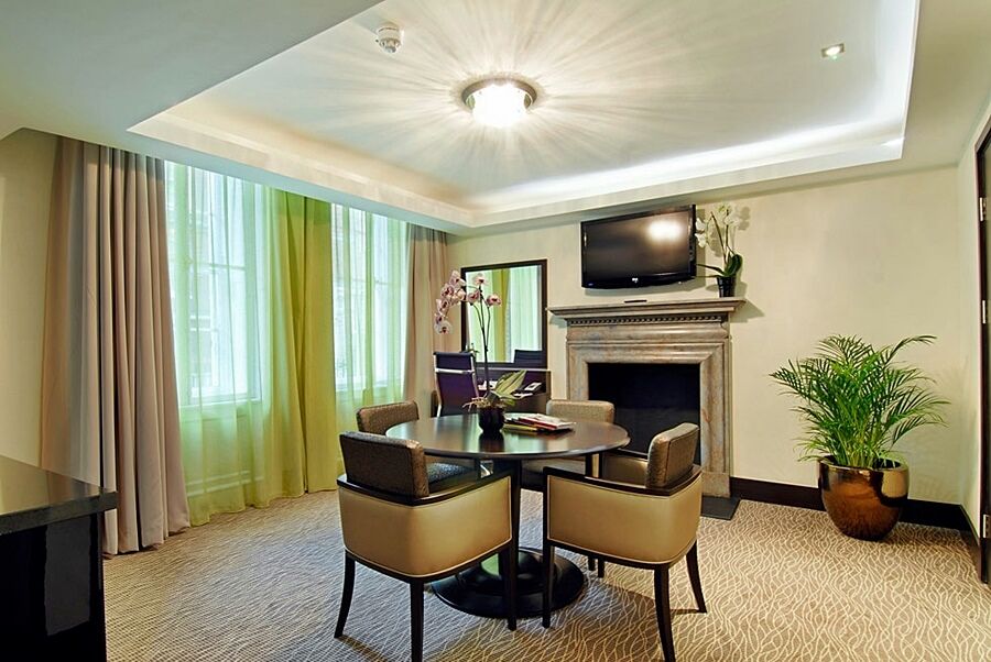 فندق Montcalm Brewery Townhouse لندن المظهر الخارجي الصورة The photo shows a well-furnished room, likely a hotel suite or a modern living space. It features a round dining table with four comfortable chairs. The walls are adorned with light-colored decor, and there are large windows with sheer and solid curt