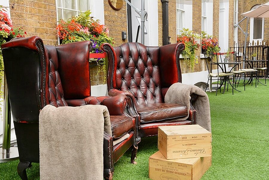 فندق Montcalm Brewery Townhouse لندن المظهر الخارجي الصورة The photo depicts two large, elegant armchairs with a classic design, featuring rich burgundy leather upholstery and button tufting. They are positioned in a cozy outdoor setting, with lush green artificial grass beneath them. Next to the chairs, the